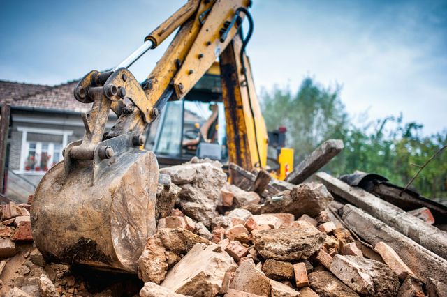 Close-up of an excavator bucket scooping brick and wood rubble from a demolished structure