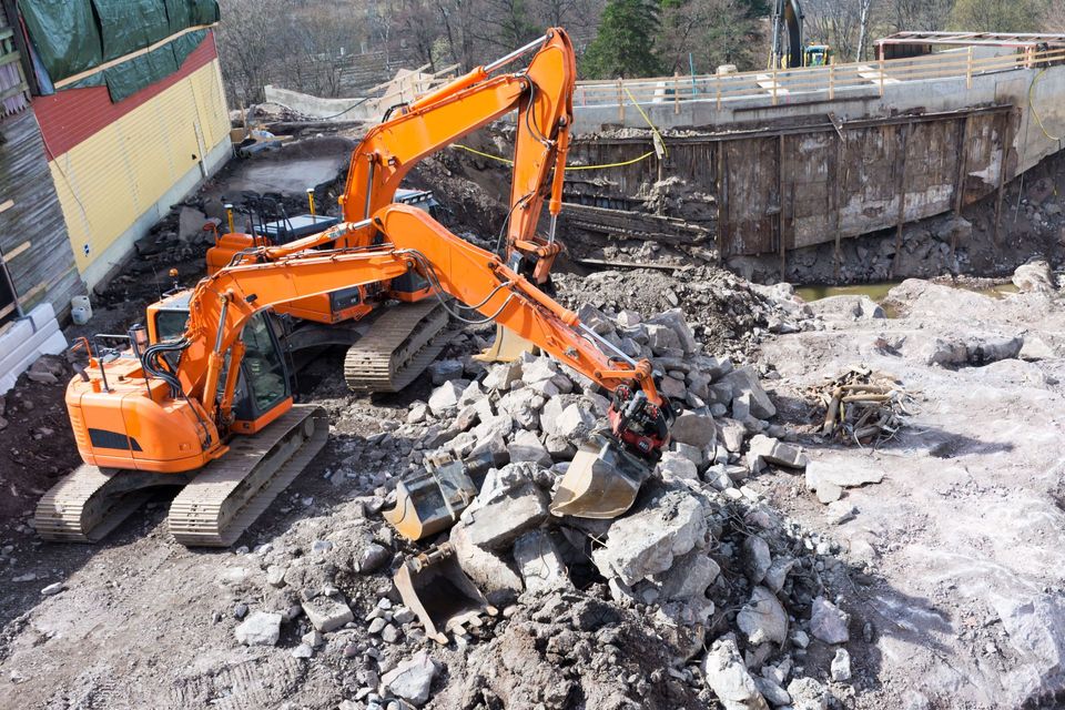 Two orange excavators breaking up concrete slabs and debris on a demolition site