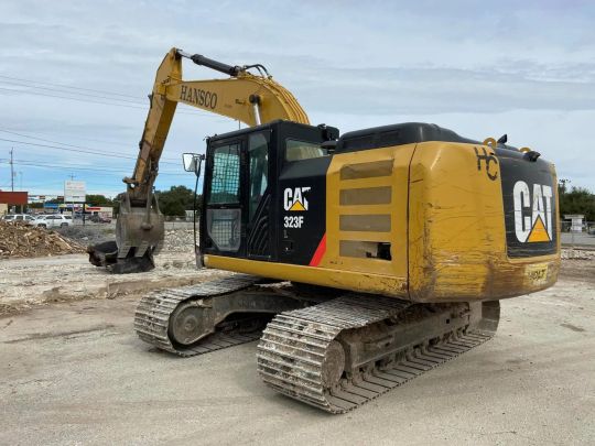 Yellow CAT 323F excavator with a Hansco boom parked on a cleared concrete lot.