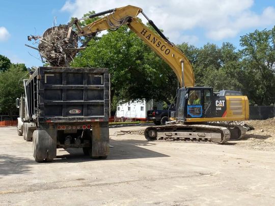 Yellow excavator loading debris into a black dump truck at a construction site.