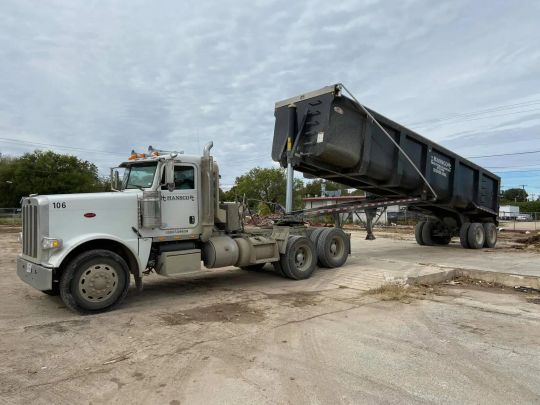 White dump truck with raised trailer on a gravel surface under a cloudy sky.