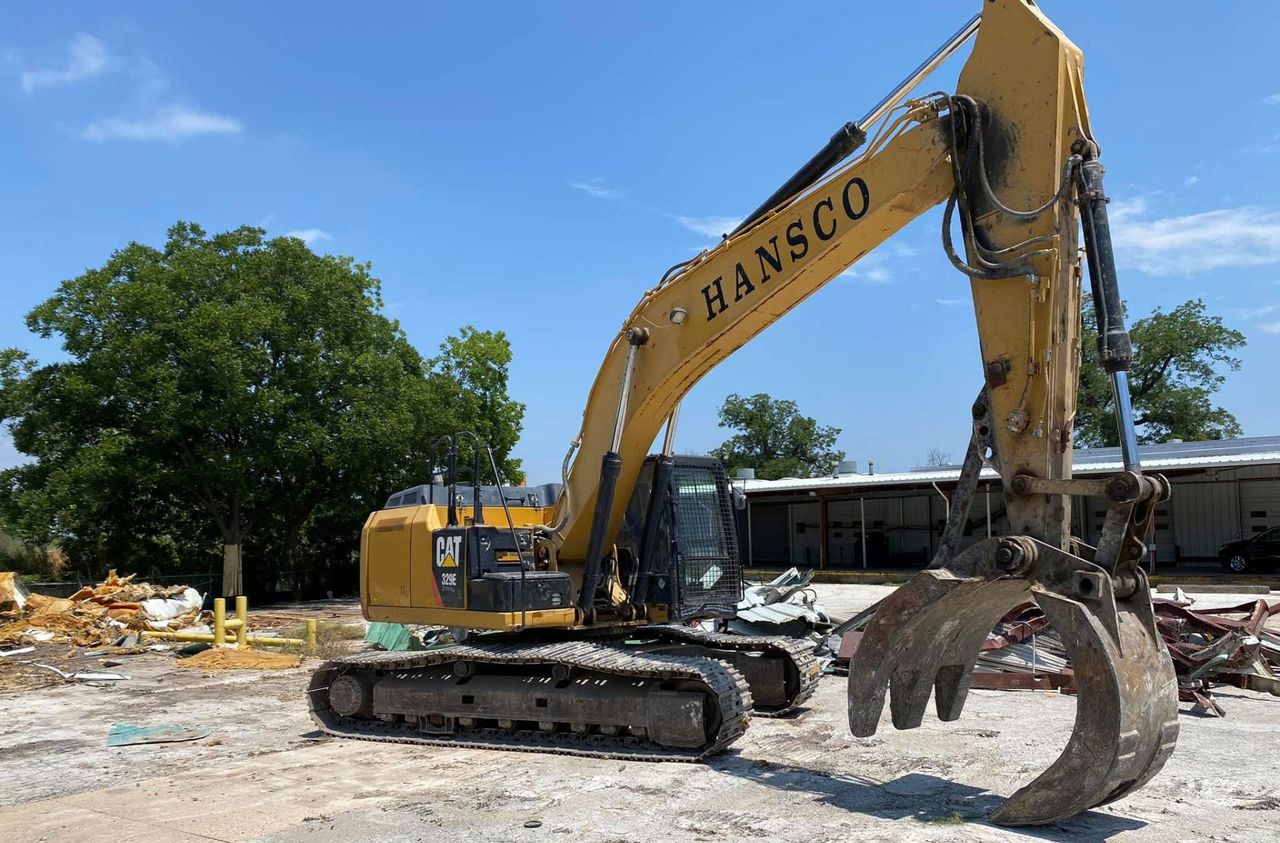 Yellow Hansco CAT excavator with a grapple attachment parked on a cleared job site