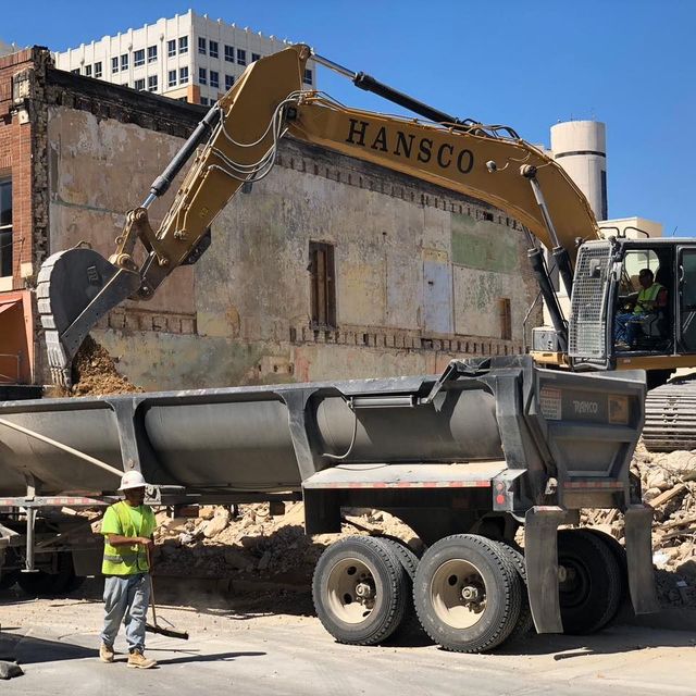 Hansco excavator loading brick debris into an end-dump trailer on a downtown demolition