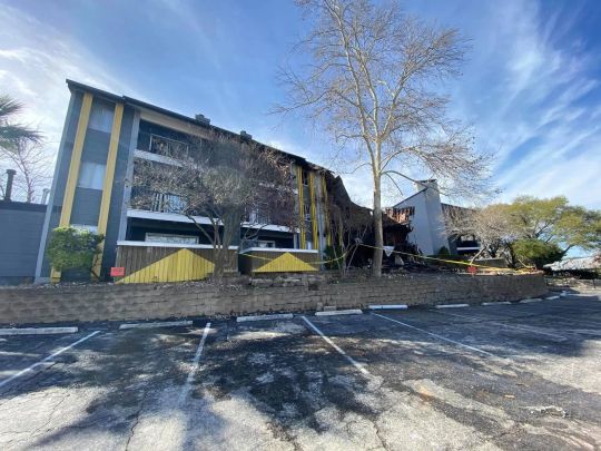 Three-story apartment complex with fire damage at one end, seen across a parking lot.