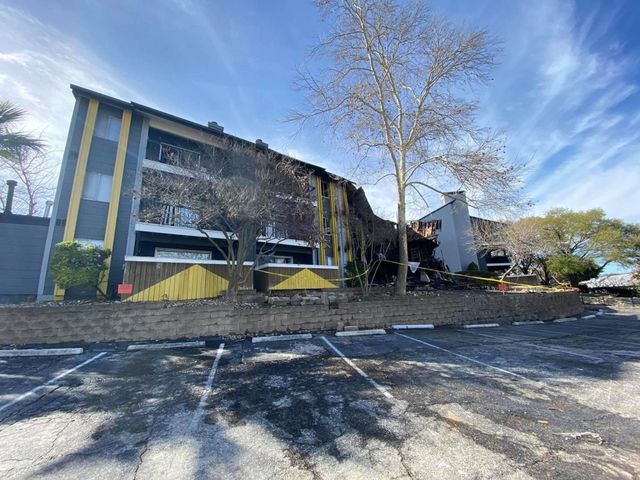 Fire-damaged apartment complex taped off behind an empty parking lot