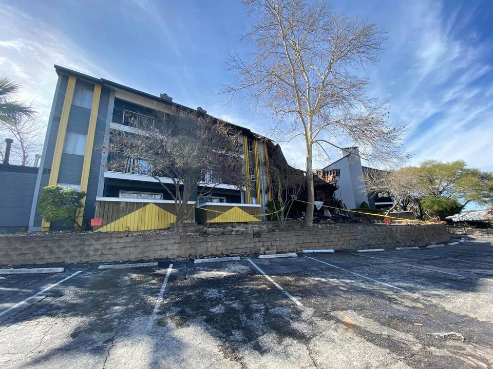 Fire-damaged apartment complex taped off behind an empty parking lot
