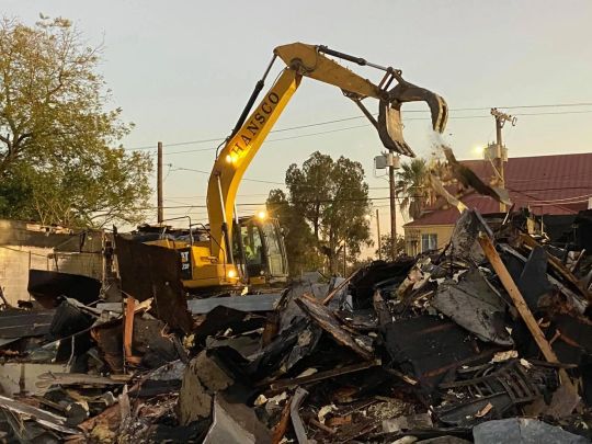 Yellow excavator demolishing debris at a construction site, daylight.