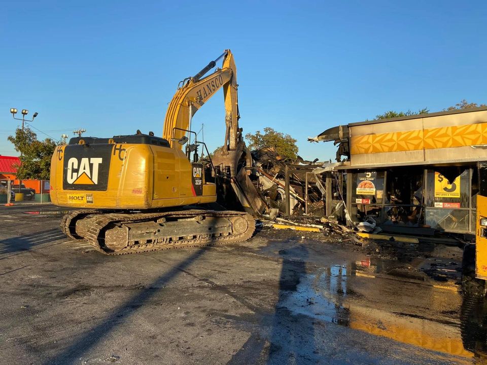 CAT excavator demolishing a commercial storefront building on a sunny morning