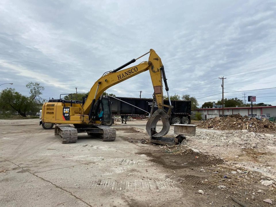 Hansco excavator with a grapple clearing concrete debris from a paved lot