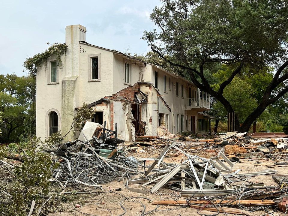 Partly deconstructed two-story stucco house with salvaged framing lumber piled out front