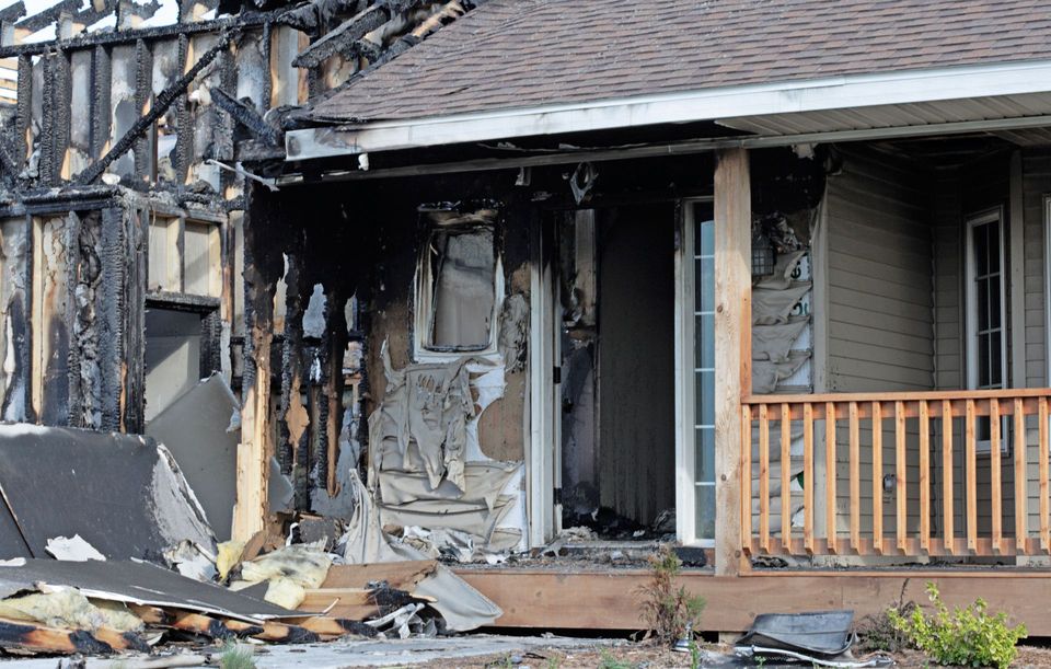 Burned-out front porch and charred siding of a fire-damaged house awaiting removal