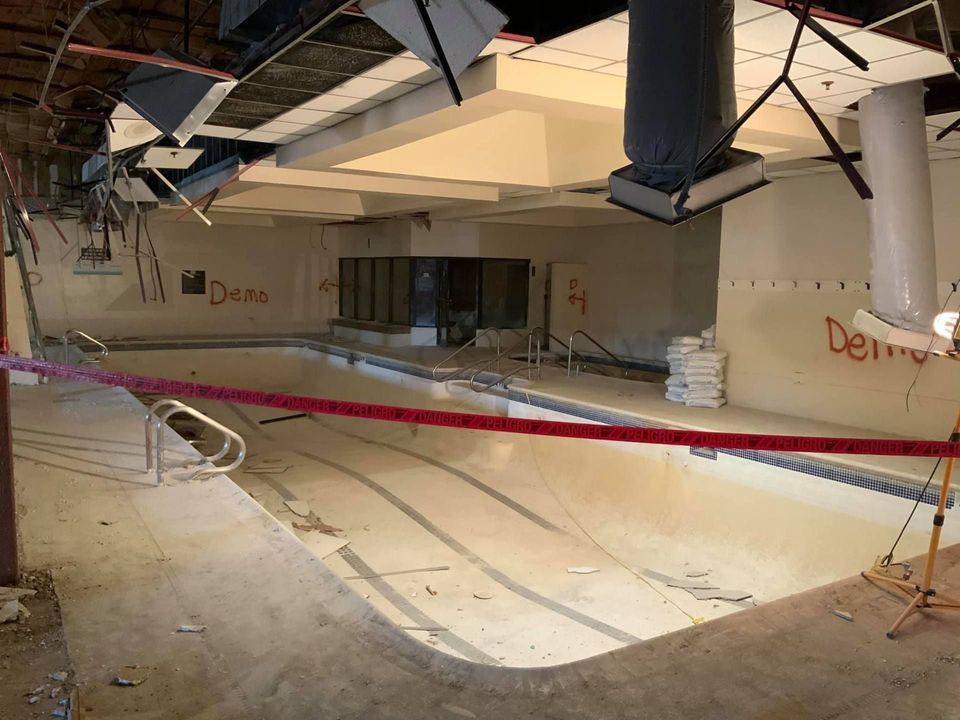 Drained indoor swimming pool taped off and marked for demolition inside a gutted building