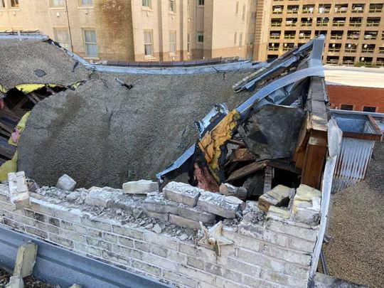 Damaged roof of a building, showing collapsed sections, bricks, and debris.