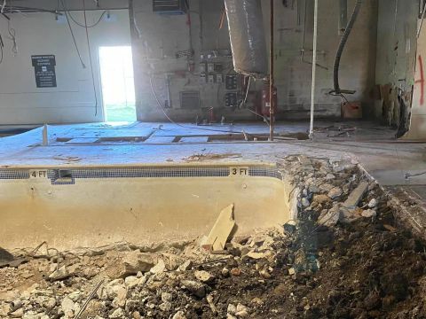 Demolished indoor pool; debris in foreground, doorway with sunlight in background.