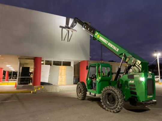 Green telehandler near a building, loading construction materials.