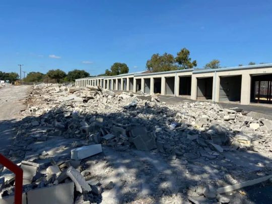 Demolished storage units with concrete debris in the foreground; blue sky.