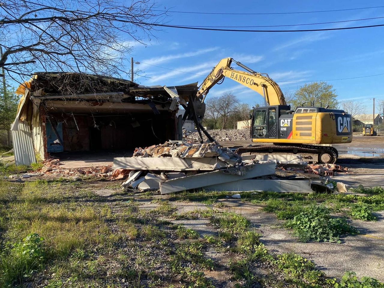 Yellow CAT excavator knocking down a building under a clear blue sky