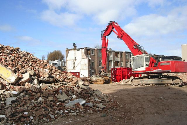 Red demolition excavator beside a large pile of brick rubble from a razed building